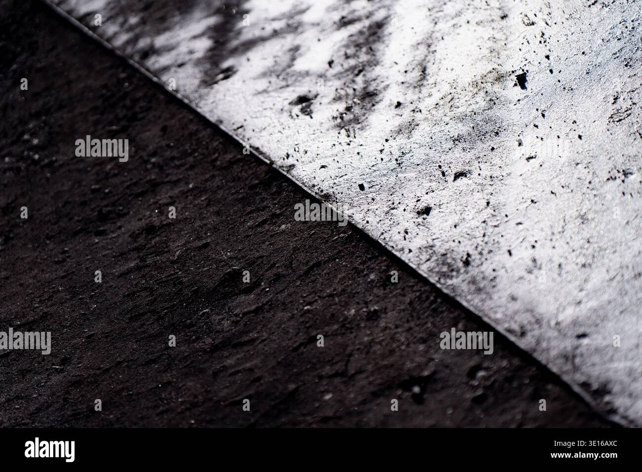 Contrasto diagonale astratto tra la superficie ruvida scura e la superficie metallica lucida, che illustra i materiali industriali, i modelli di usura e il design Foto Stock