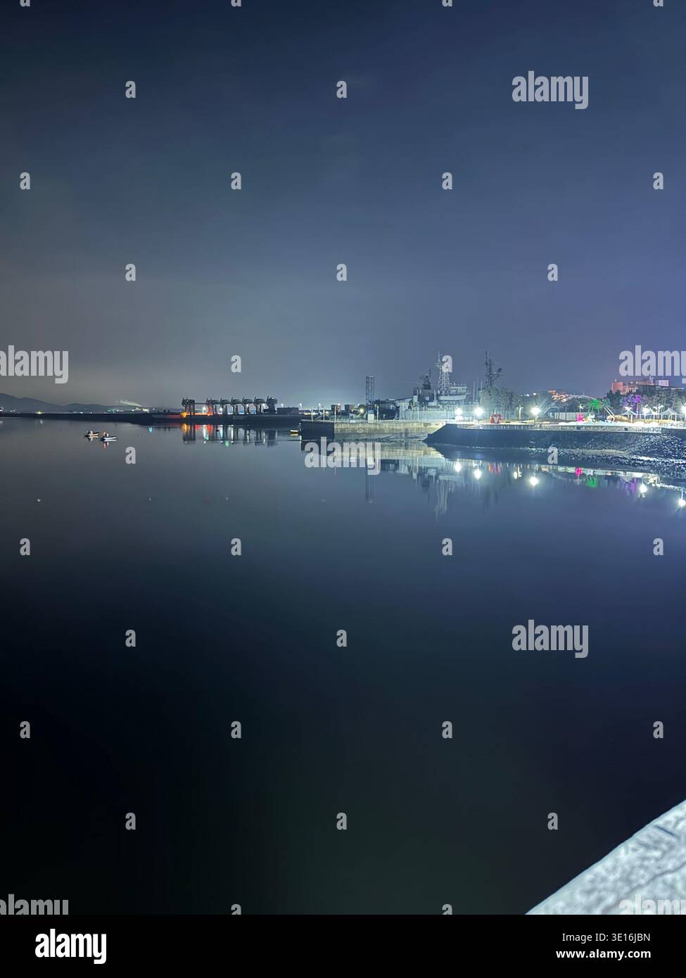 Porto illuminato di notte con nave e luci colorate che si riflettono sul mare calmo della Corea del Sud - Immagine stock catturata con smartphone