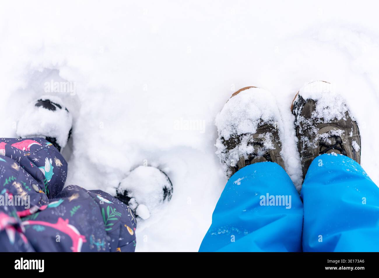 Padre e figlio stanno insieme nella neve fresca, i loro stivali invernali spolverati di bianco Foto Stock