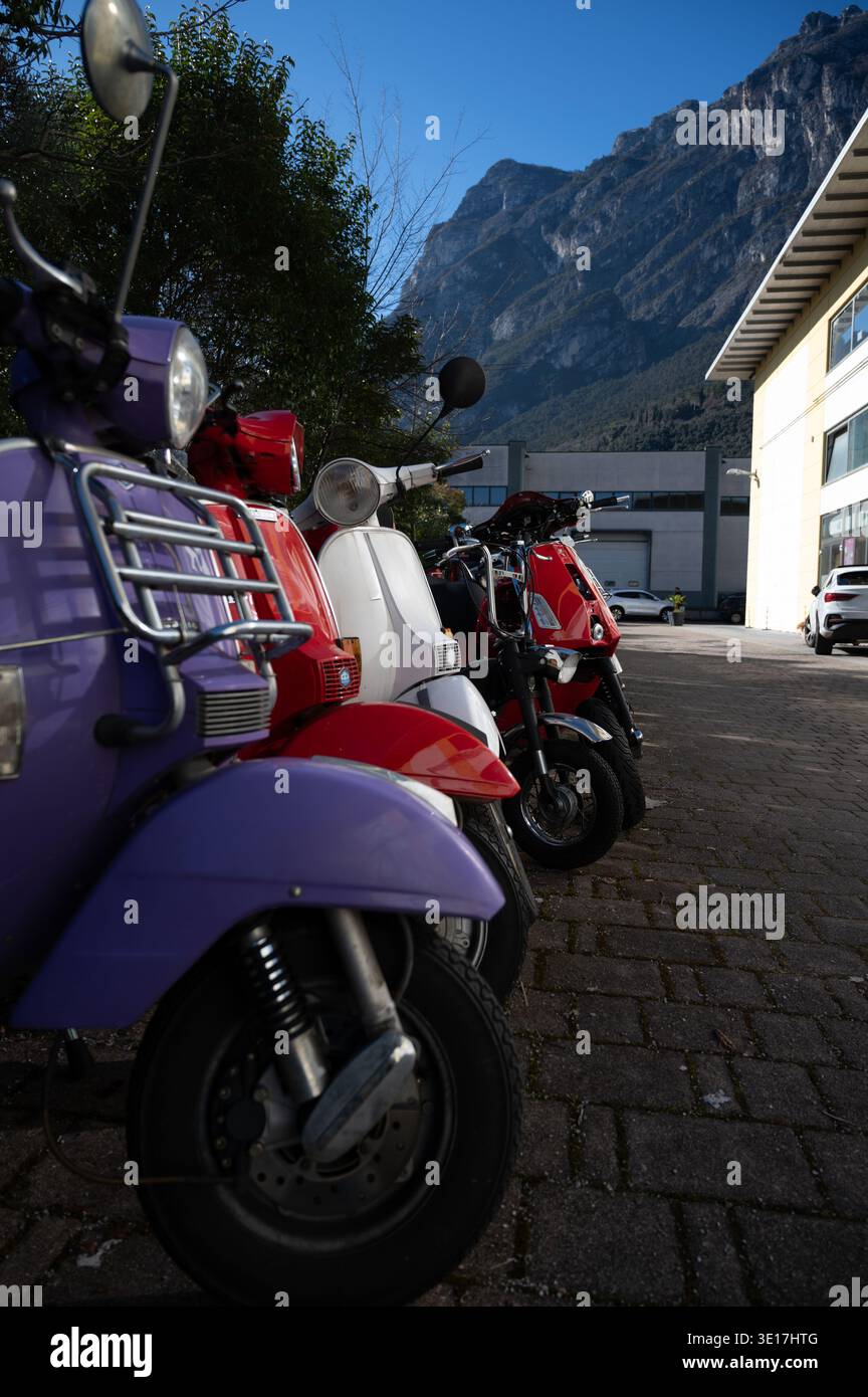 Una linea di scooter vibranti è parcheggiata accanto a un edificio a Malcesine, con lo splendido sfondo del Lago di Garda e delle montagne circostanti in Italia unde Foto Stock