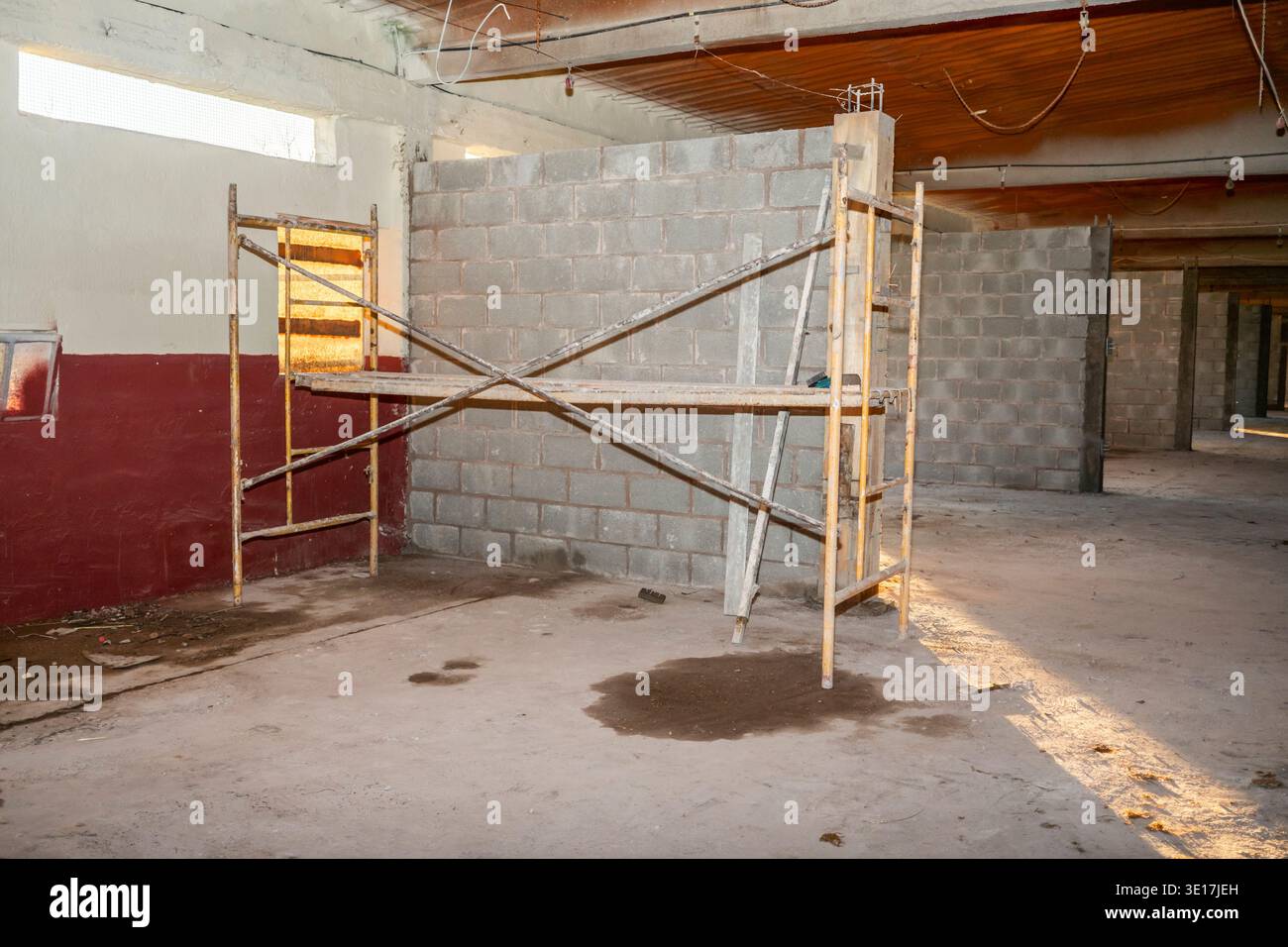 Un cantiere con impalcature e un muro di cemento parzialmente costruito. L'impostazione interna visualizza l'avanzamento in muratura e lavori strutturali unde Foto Stock