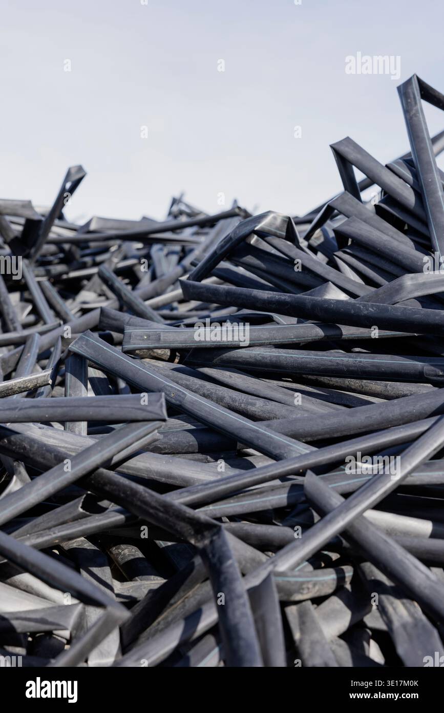 Un'ampia pila di tubi di irrigazione in polietilene nero pronti per il riciclaggio. I tubi, impilati sotto un cielo limpido, rappresentano il processo di sostentamento Foto Stock
