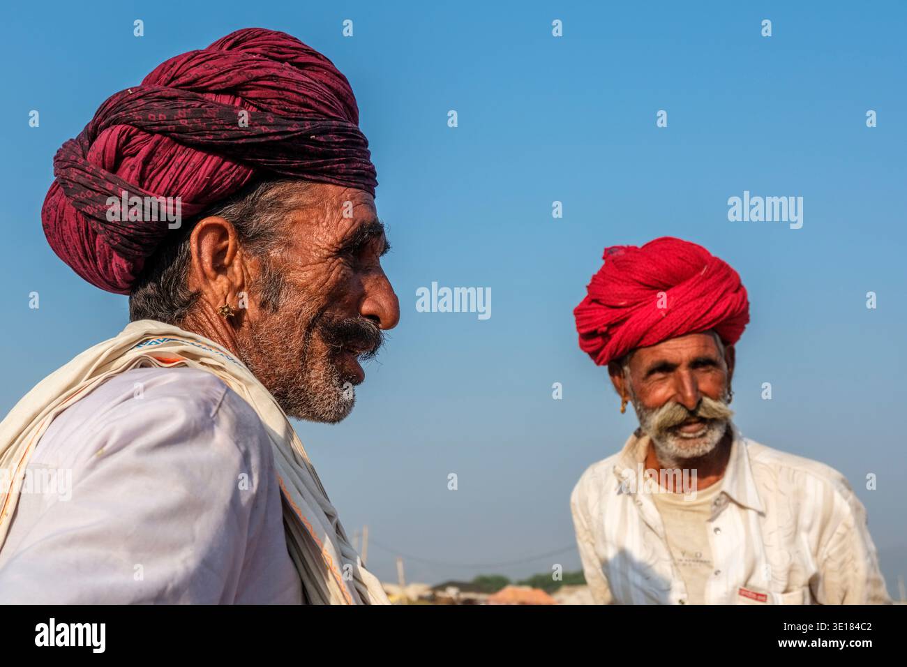 Due uomini che indossano turbanti dai colori vivaci guardano in direzioni diverse contro un cielo blu chiaro durante l'annuale Fiera dei cammelli di Pushkar. Foto Stock