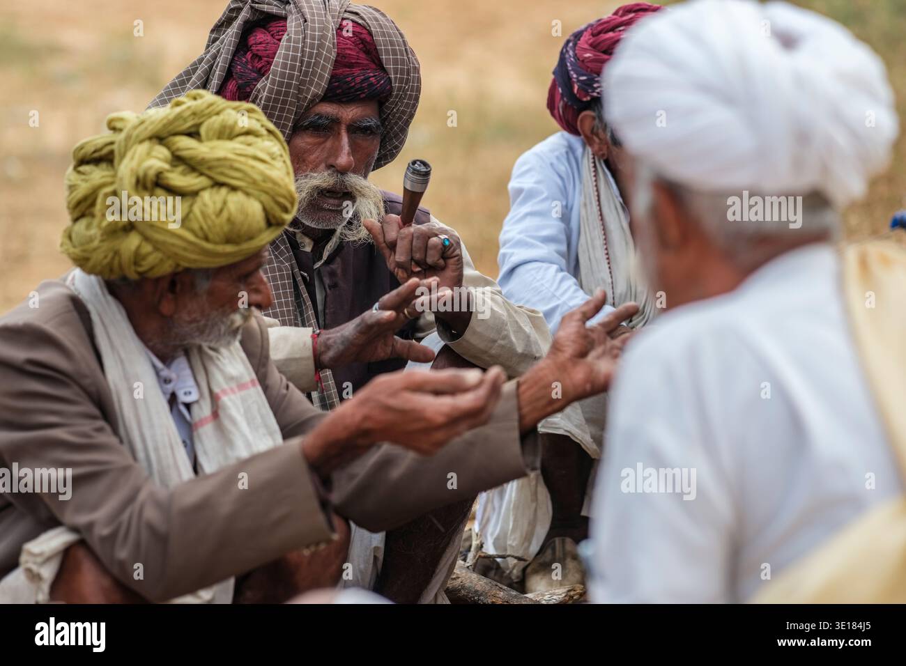 Un gruppo di uomini che indossano vari turbanti tradizionali si siedono insieme e conversano alla Fiera dei cammelli di Pushkar, mentre un uomo tiene una piccola pipa. Foto Stock