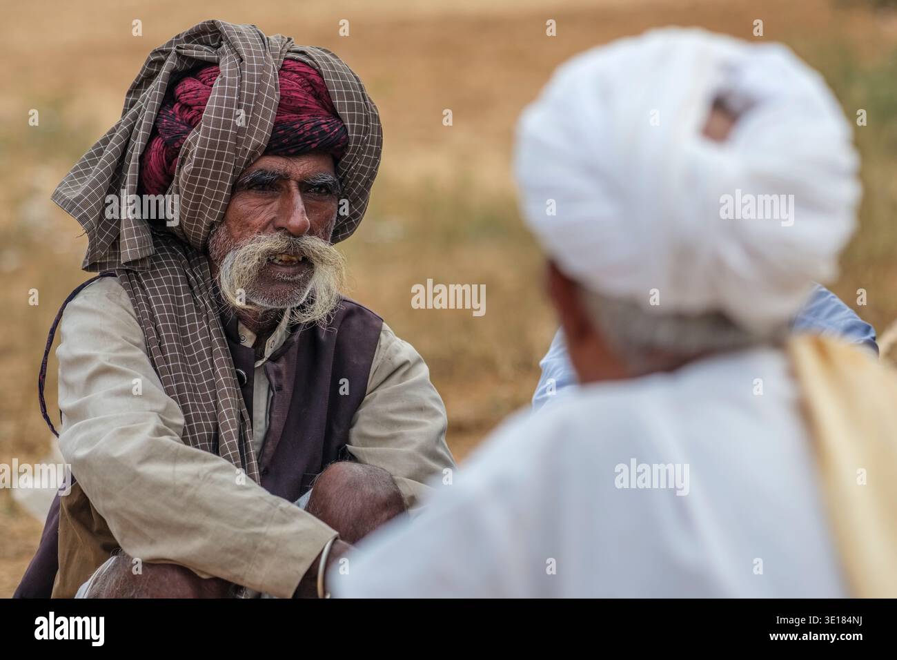Durante la Fiera dei cammelli di Pushkar, un uomo con un turbante a scacchi e grandi baffi grigi parla con un'altra persona la cui schiena è alla telecamera. Foto Stock