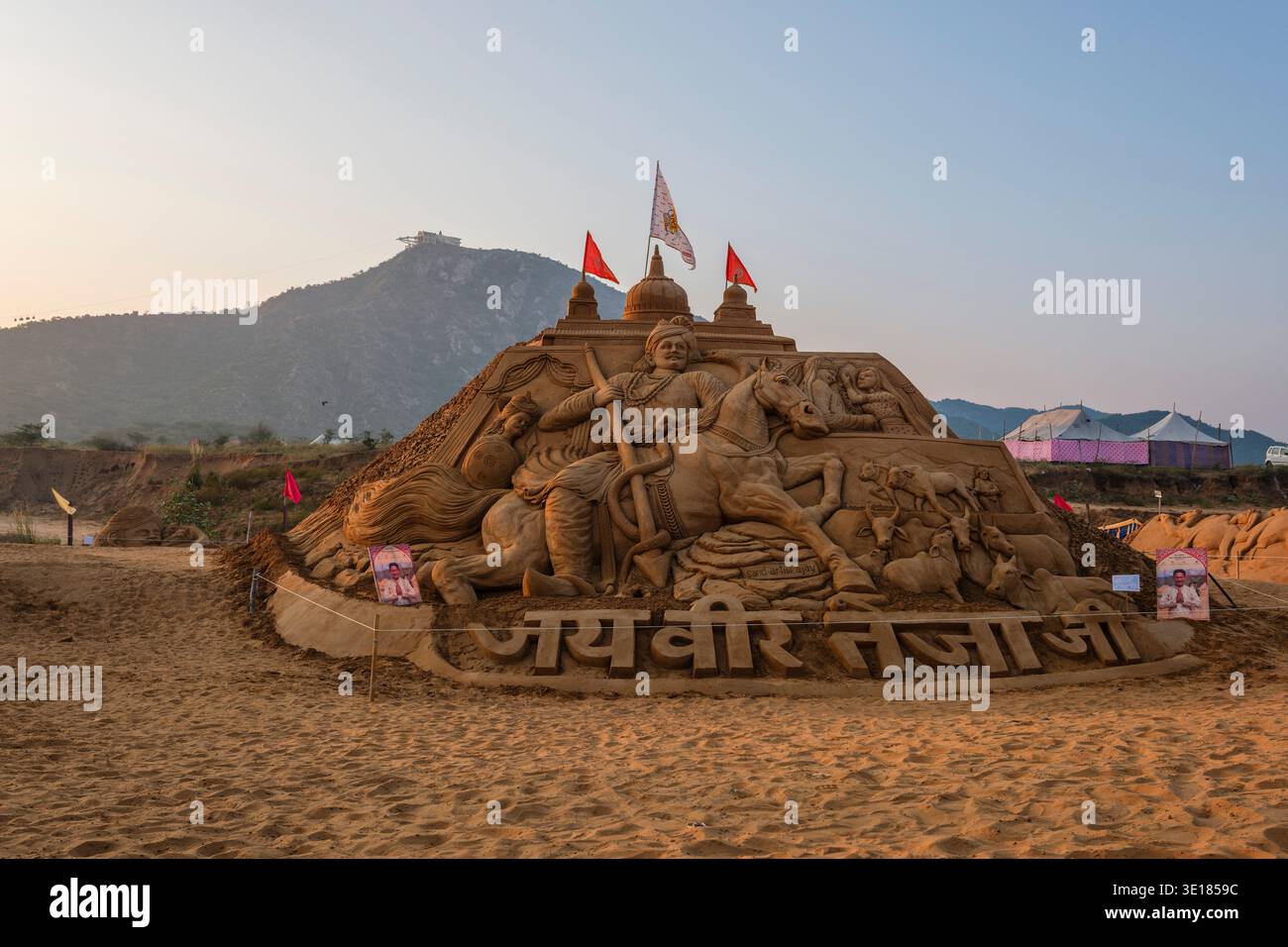 Una grande scultura di sabbia raffigurante un guerriero su un cavallo si erge presso la Fiera dei cammelli di Pushkar, con una collina e un tempio visibili in lontananza. Foto Stock
