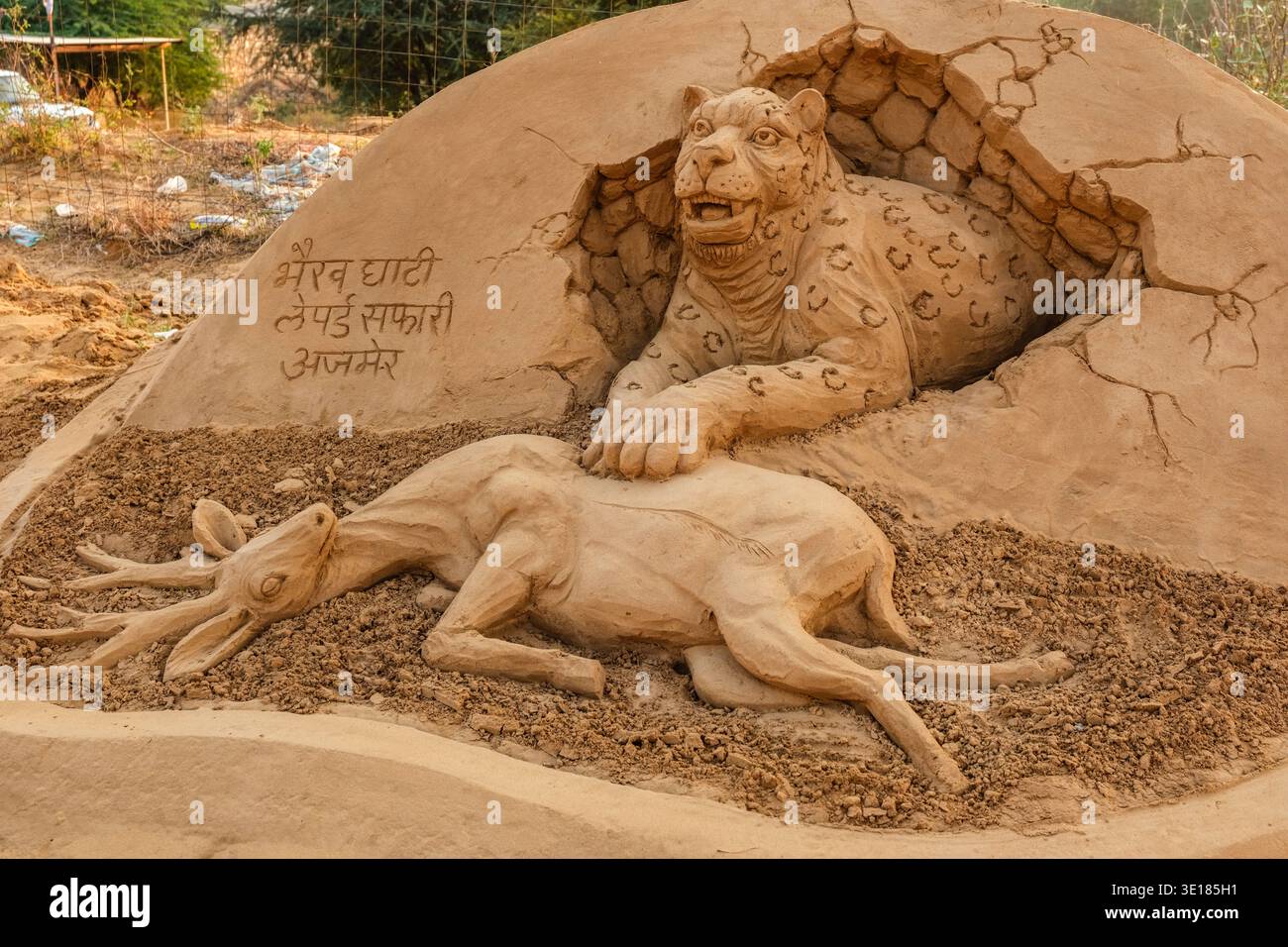 Un'installazione di arte di sabbia per la Fiera dei cammelli di Pushkar mostra un leopardo che emerge da una buca per cacciare un cervo, con iscrizioni Hindi. Foto Stock