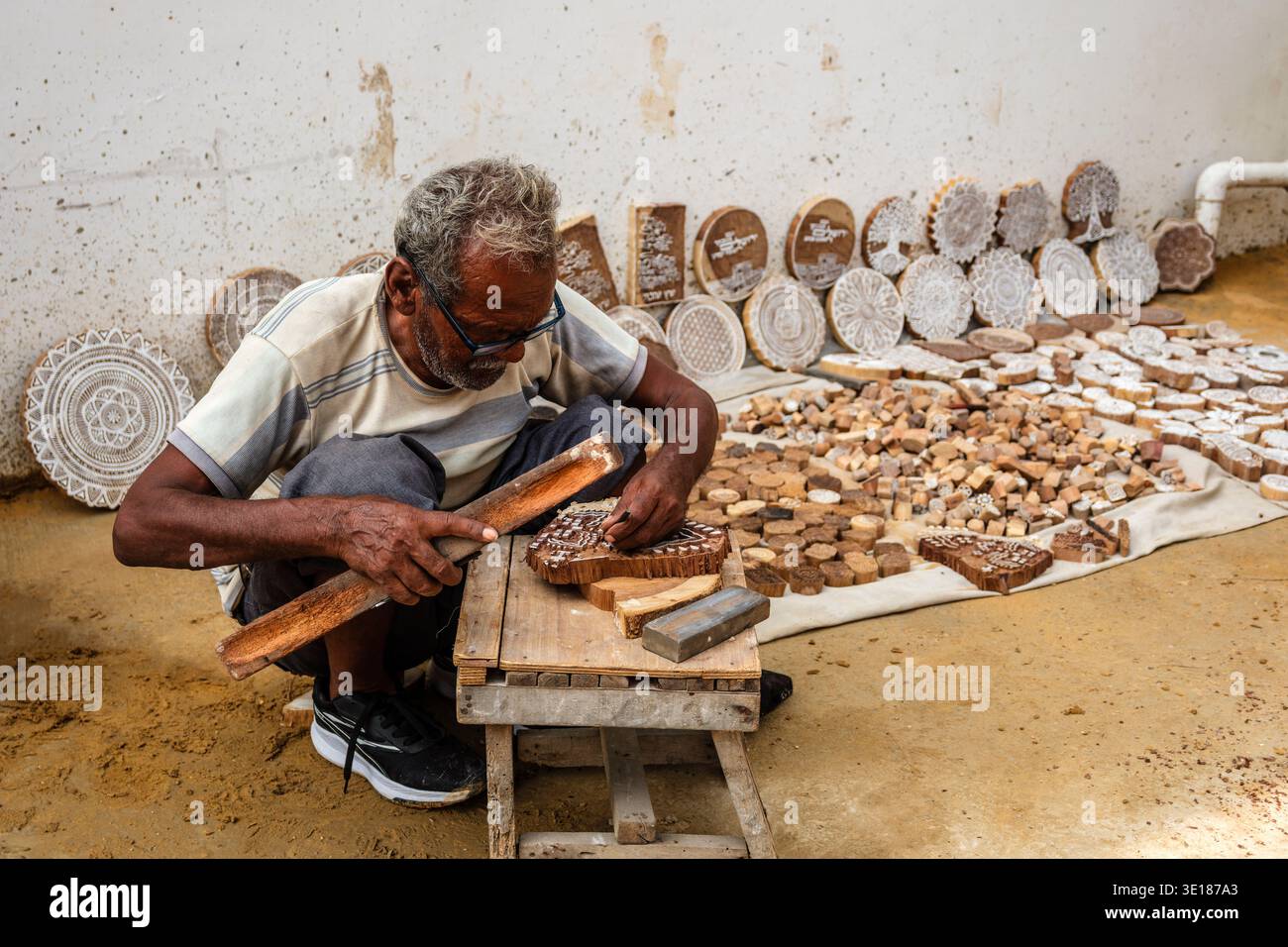 Un artigiano di Pushkar Mela scava su una bassa panchina di legno, usando un piccolo strumento per intagliare intricatamente i tradizionali motivi floreali in un blocco di legno. Foto Stock