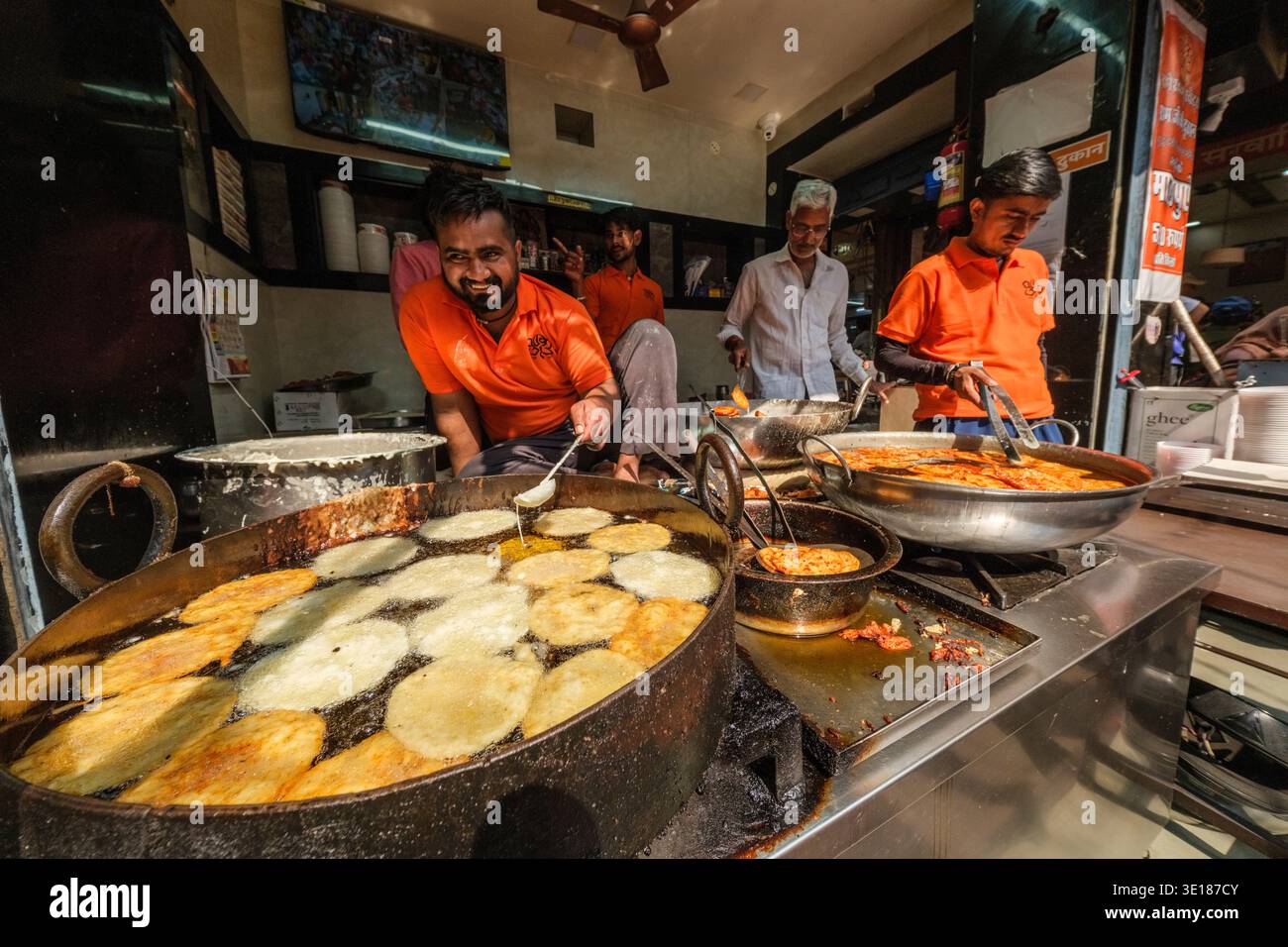 Cuoce in camicie arancioni brillanti friggono grandi quantità di focaccine dorate in olio profondo in un affollato chiosco di cibo di strada durante l'annuale festival Pushkar Mela. Foto Stock