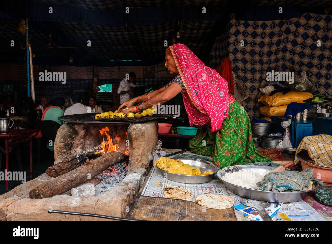 Una donna al Pushkar Mela prepara con cura delle palle di impasto gialle su una grande piastra circolare sopra un fuoco a legna aperto all'interno di una tenda in tessuto a motivi geometrici. Foto Stock