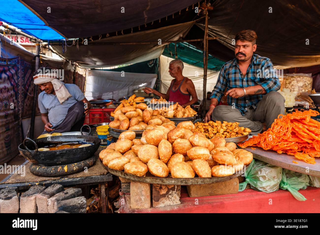 I venditori di Pushkar Mela si trovano dietro tumuli di kachori fritti e di jalebi di arancia brillante, mentre un altro uomo prepara l'impasto fresco in lontananza. Foto Stock