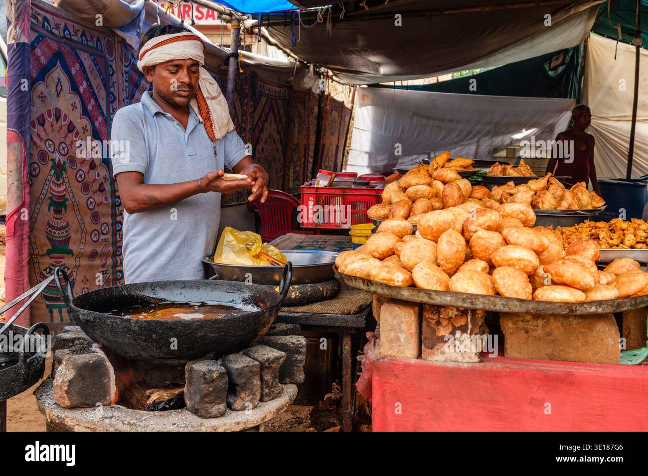In un chiosco di cibo di Pushkar Mela, un uomo con un velo bianco forma l'impasto a mano accanto a un grande wok di ferro e un vassoio pieno di pasticcini fritti. Foto Stock