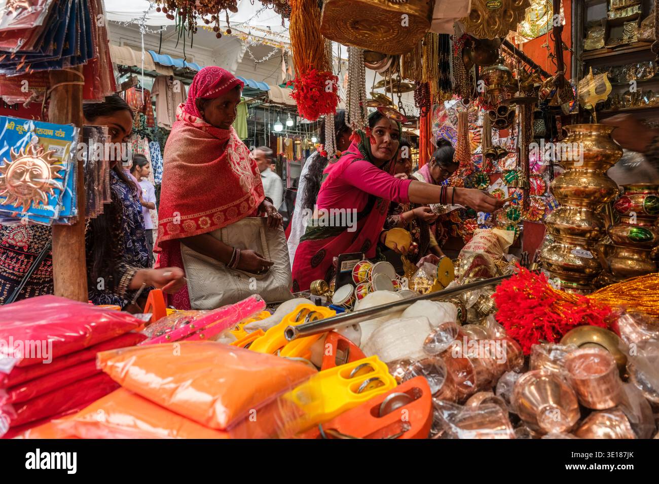 Le donne in colorato saris curiosano tra le affollate bancarelle del mercato di Pushkar Mela, piene di pentole di ottone, campane e articoli rituali sotto un baldacchino bianco. Foto Stock