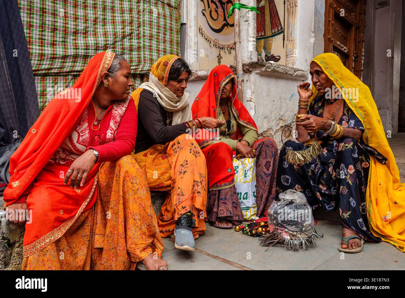 Quattro donne vestite con abiti tradizionali Rajasthani siedono su un gradino di pietra a Pushkar Mela, discutendo di gioielli mentre una porta ornata si trova nelle vicinanze. Foto Stock