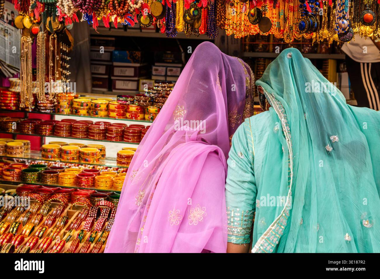 Due donne in veli viola e turchese traslucidi guardano un'ampia esposizione di bracciali in vetro e collane con perline in uno stand di Pushkar Mela. Foto Stock
