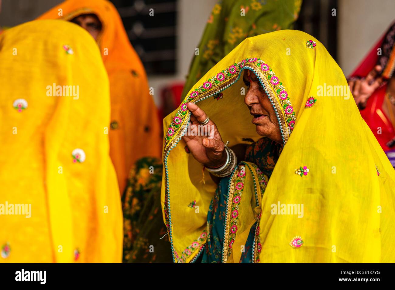 Una donna di Pushkar Mela regola il suo velo ricamato giallo mentre parla, un'altra persona in arancione si siede in lontananza. Foto Stock