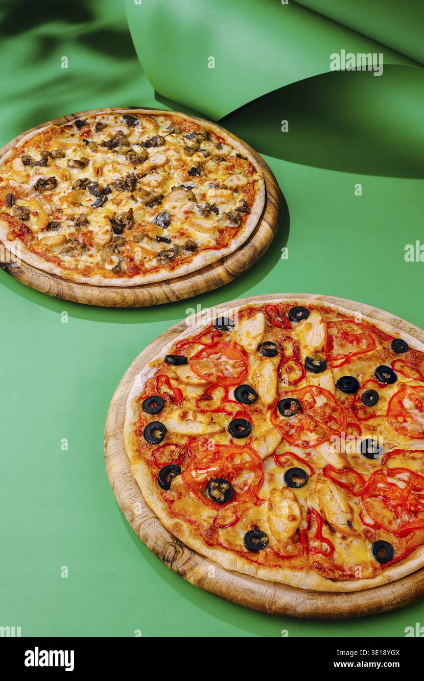 Due pizze rotonde con vari condimenti sono esposte su vassoi di legno. Una comprende olive e peperoni, mentre l'altra comprende funghi e formaggi, Foto Stock