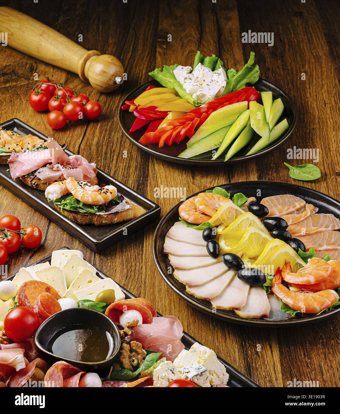 Delizioso assortimento di antipasti esposti su un tavolo di legno che comprende gamberi, affettati, formaggi, peperoni, pomodori, olive e verdure fresche. IDE Foto Stock
