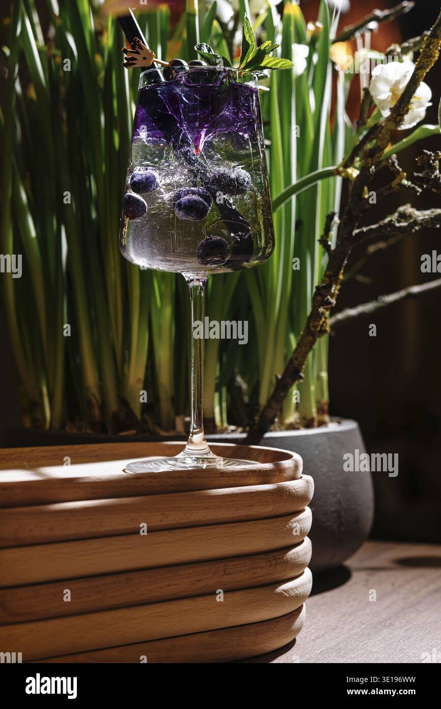 Cocktail rinfrescante con mirtilli e menta, guarnito con un fiore commestibile, servito su un vassoio di legno Foto Stock