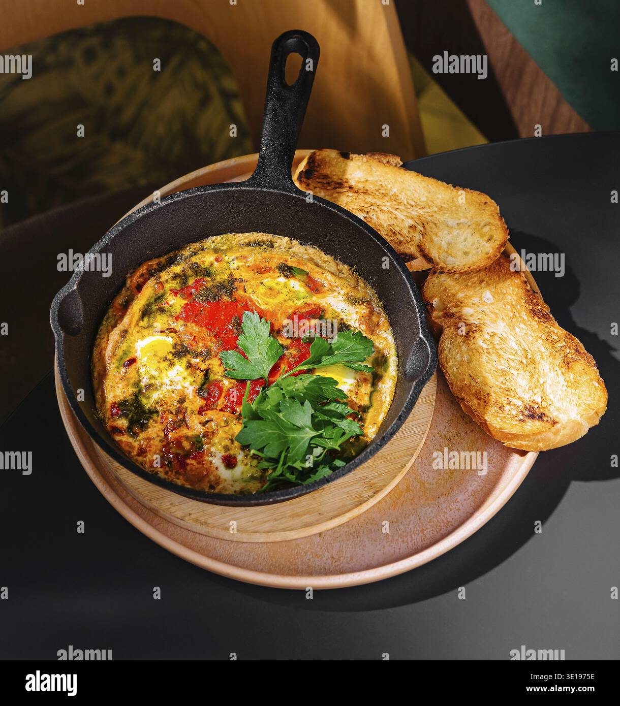 Uova appena cucinate con verdure ed erbe aromatiche servite su vassoio di legno con pane tostato su un tavolo nero nel caffè Foto Stock