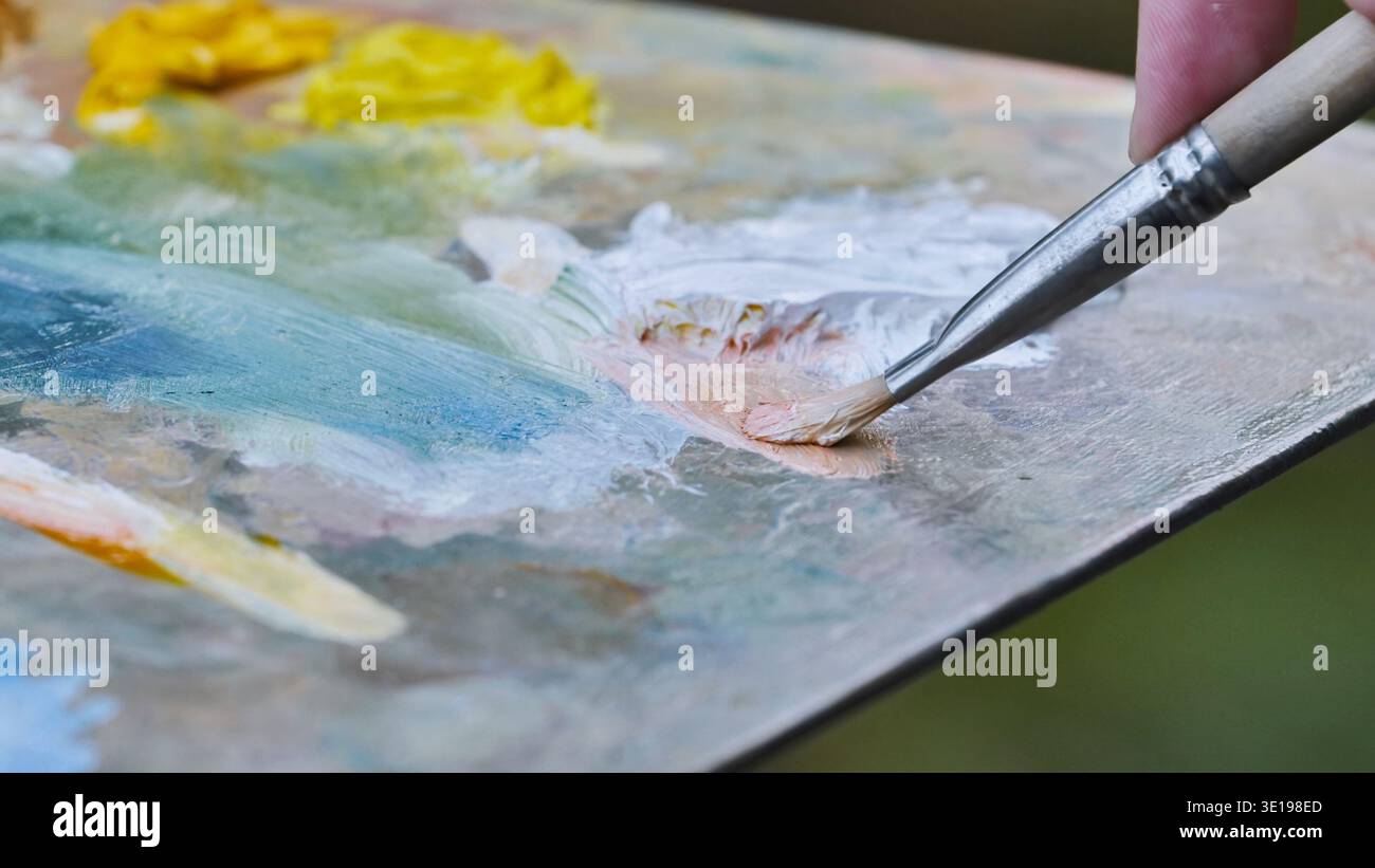 L'artista mescola le vernici a olio sulla tavolozza con il pennello per creare un nuovo colore Foto Stock