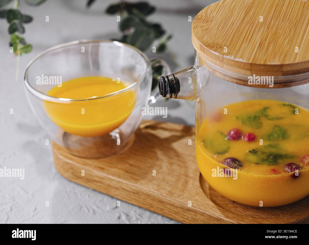 Caraffa di vetro piena di acqua infuso con agrumi, guarnita con frutti di bosco su un vassoio di legno Foto Stock