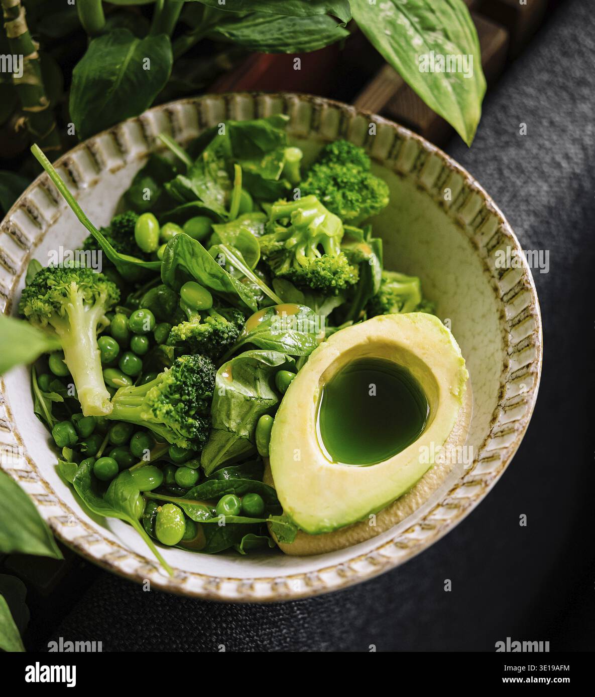 Insalata verde vivace con avocado maturo, broccoli, piselli e verdure miste in un recipiente di ceramica Foto Stock