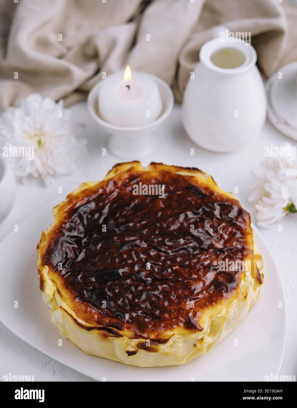 Cheesecake basca bruciata splendidamente presentata con luci soffuse e un sofisticato arredamento da tavolo Foto Stock