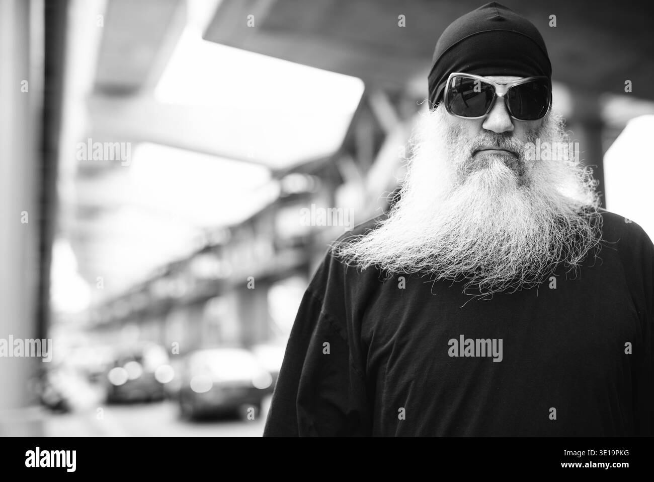 Ritratto di un uomo hipster barbuto maturo con cappello a berretto nelle strade della città all'aperto in bianco e nero Foto Stock