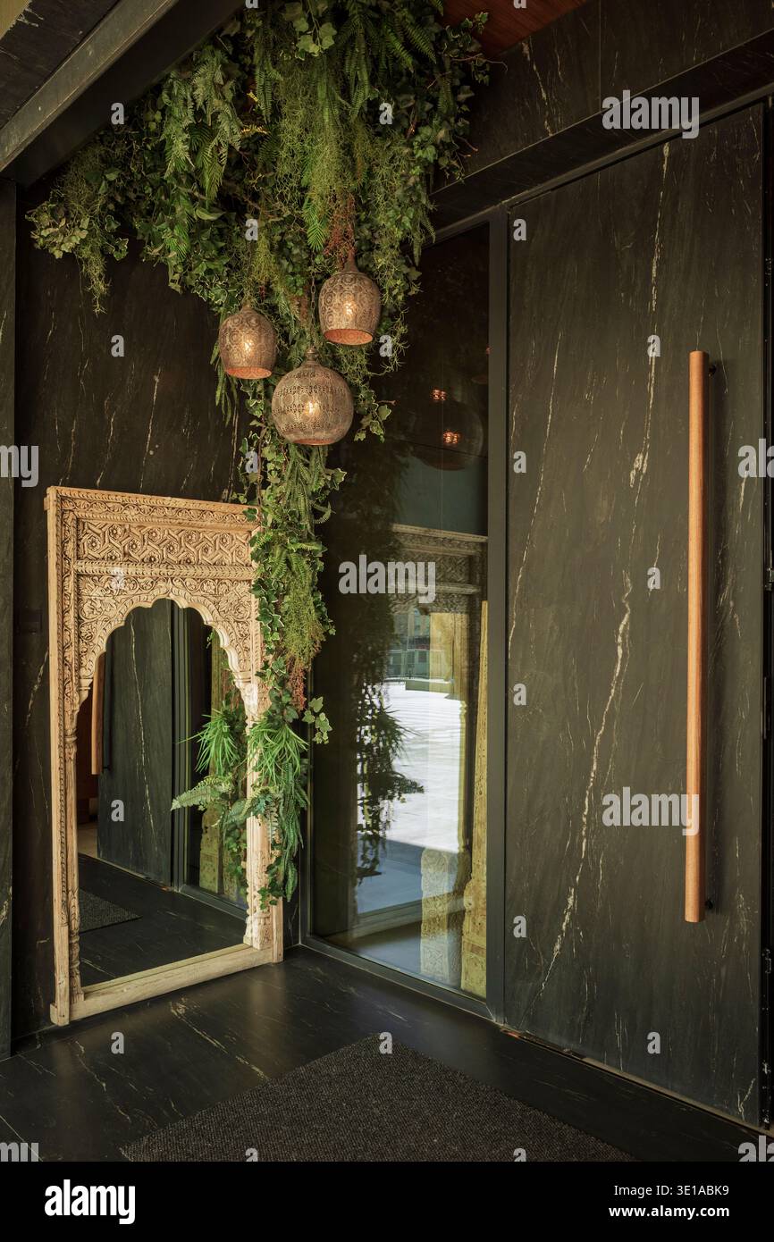 Elegante ingresso del Restaurante El Ceramista a Vila-Real, Spagna, caratterizzato da pareti in marmo scuro, lussureggianti piante appese, specchi ornati e calde lanterne. Foto Stock