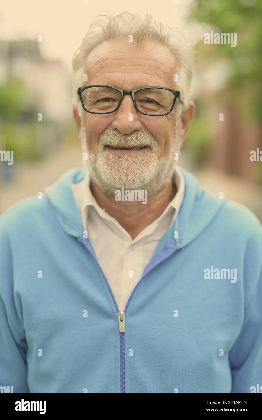Faccia di felice bello senior barbuto uomo sorridente indossando giacca blu e occhiali all'aperto Foto Stock
