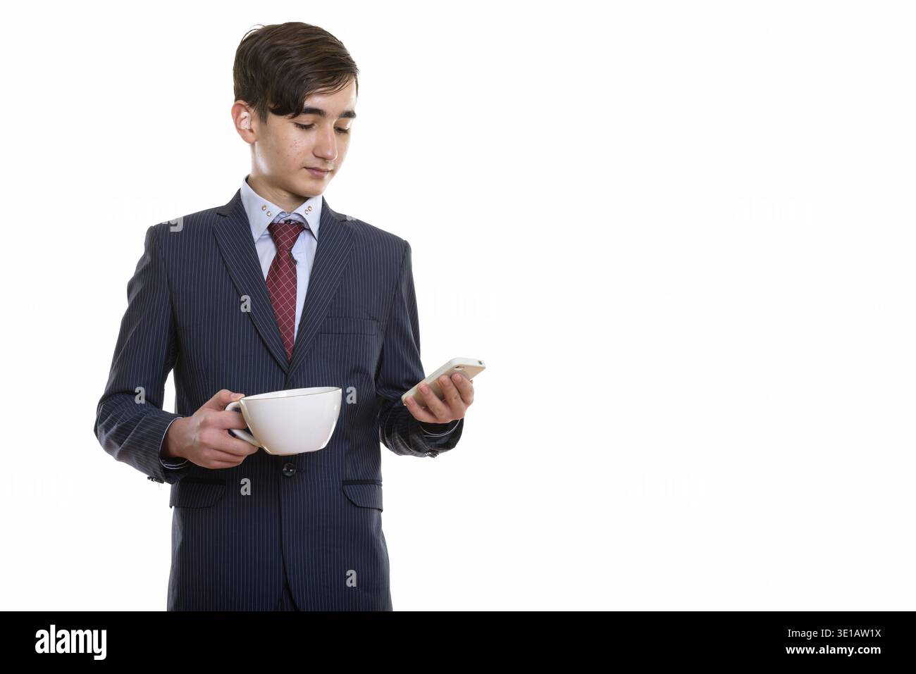 Studio shot di giovane bel ragazzo persiano uomo d'affari che tiene il caffè cup e utilizzando il telefono cellulare Foto Stock