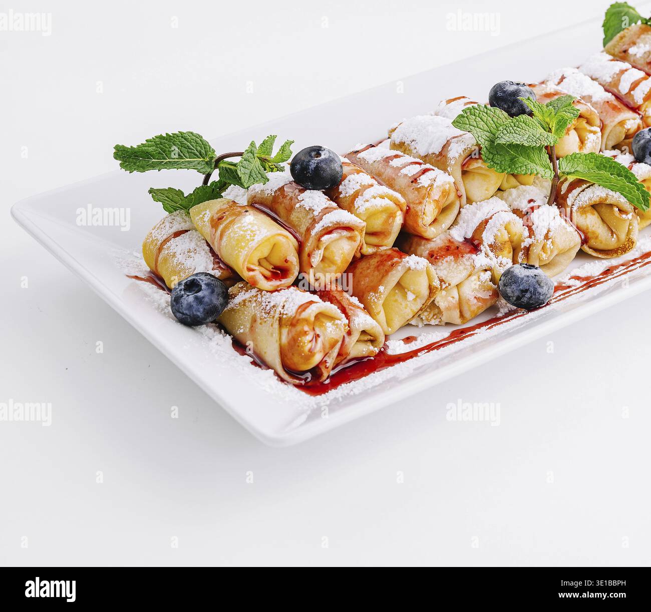 Deliziose mini pancake condite con sciroppo, spolverate con zucchero a velo e guarnite con frutti di bosco freschi e foglie di menta Foto Stock