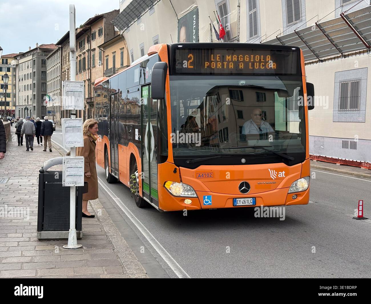 Autobus della linea 2 che arriva a Pisa, Italia. La donna aspetta alla fermata dell'autobus accanto agli edifici storici, luogo di transito urbano comune europeo. Foto Stock