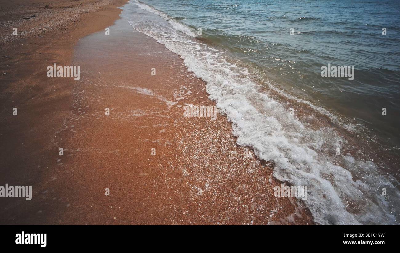 Onde delicate che scivolano su sabbia dorata su una spiaggia soleggiata in crimea, creando un paesaggio marino tranquillo e invitante Foto Stock