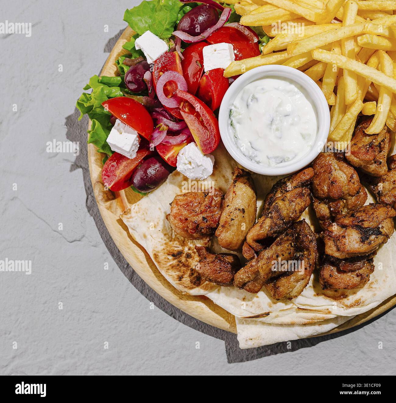 Un piatto vivace con pollo alla griglia, verdure fresche, patatine fritte e salsa tzatziki. L'insalata colorata include pomodori, lattuga, olive Foto Stock