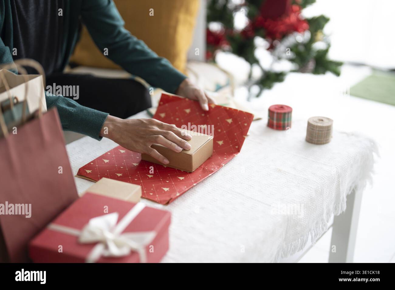 Uomo in maglione che avvolge i regali di natale con carta ecologica da ragazza che confeziona regali di natale concetto natalizio Foto Stock