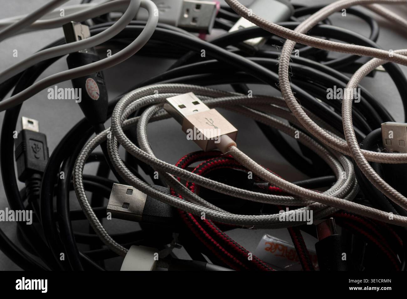 Primo piano di cavi USB aggrovigliati e cavi di ricarica che formano una serie disordinata di accessori e connettori elettronici. Foto Stock