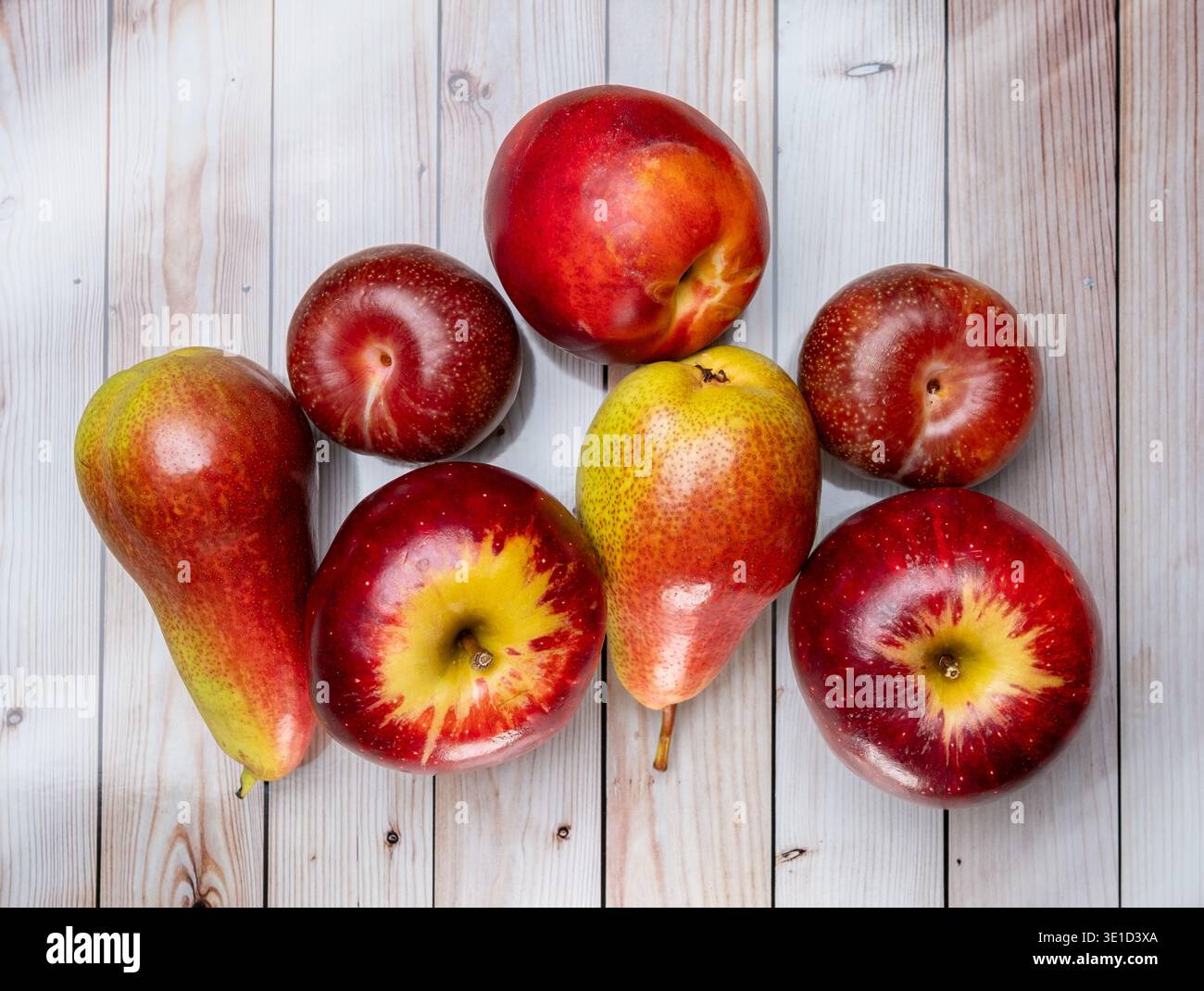 Variopinto assortimento di frutta fresca, tra cui mele rosse, pere mature e frutta di pietra disposte su tavole di legno bianche rustiche. Rosso vivo, giallo, AN Foto Stock