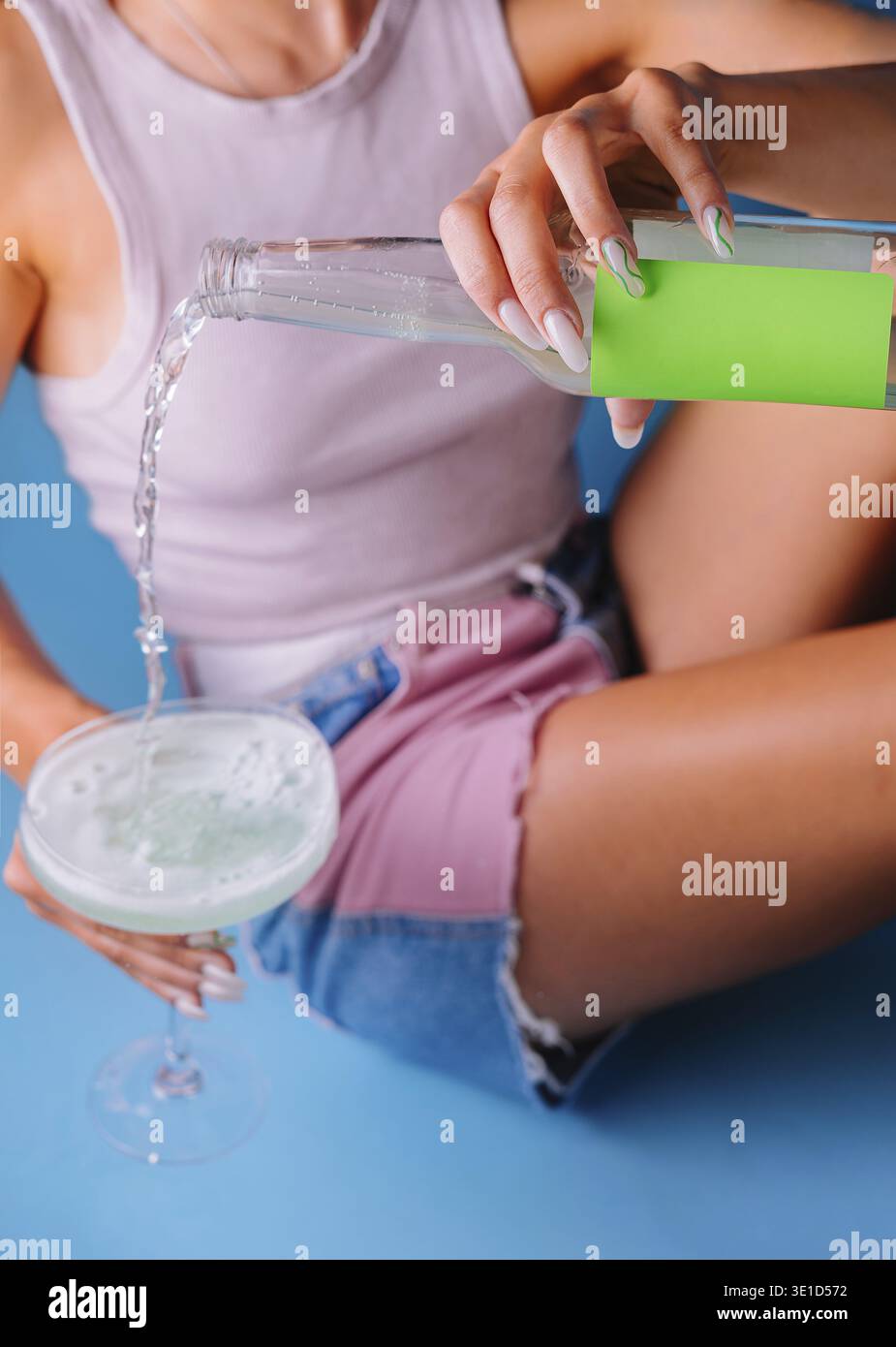 Una giovane donna sta versando una bevanda verde da una bottiglia con un'etichetta di mockup in un bicchiere Foto Stock