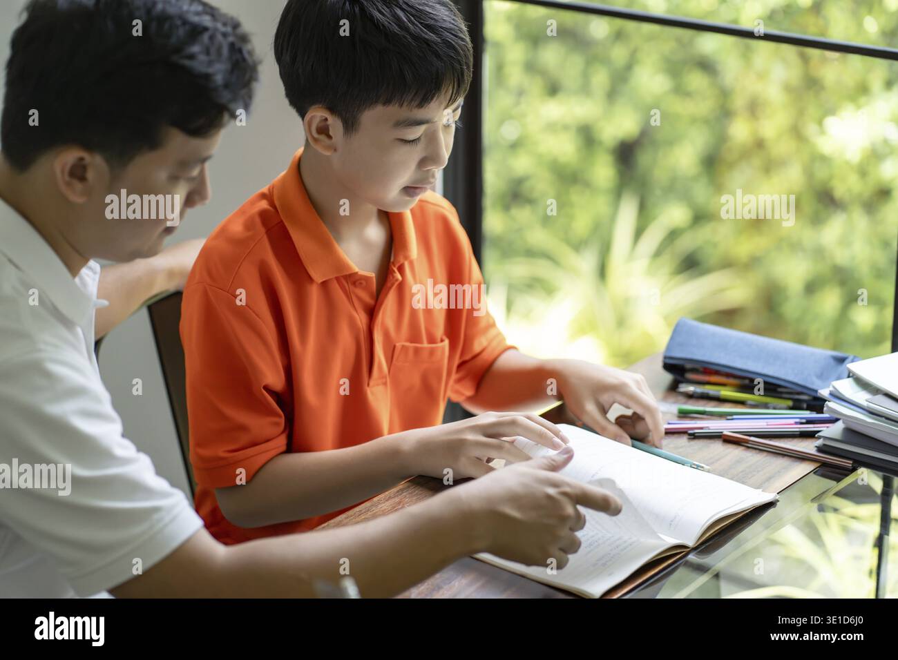 Il padre asiatico aiuta il figlio a fare i compiti per la scuola. i bambini studiano insieme concetto di scuola a casa ricevendo l'aiuto del padre per i compiti Foto Stock