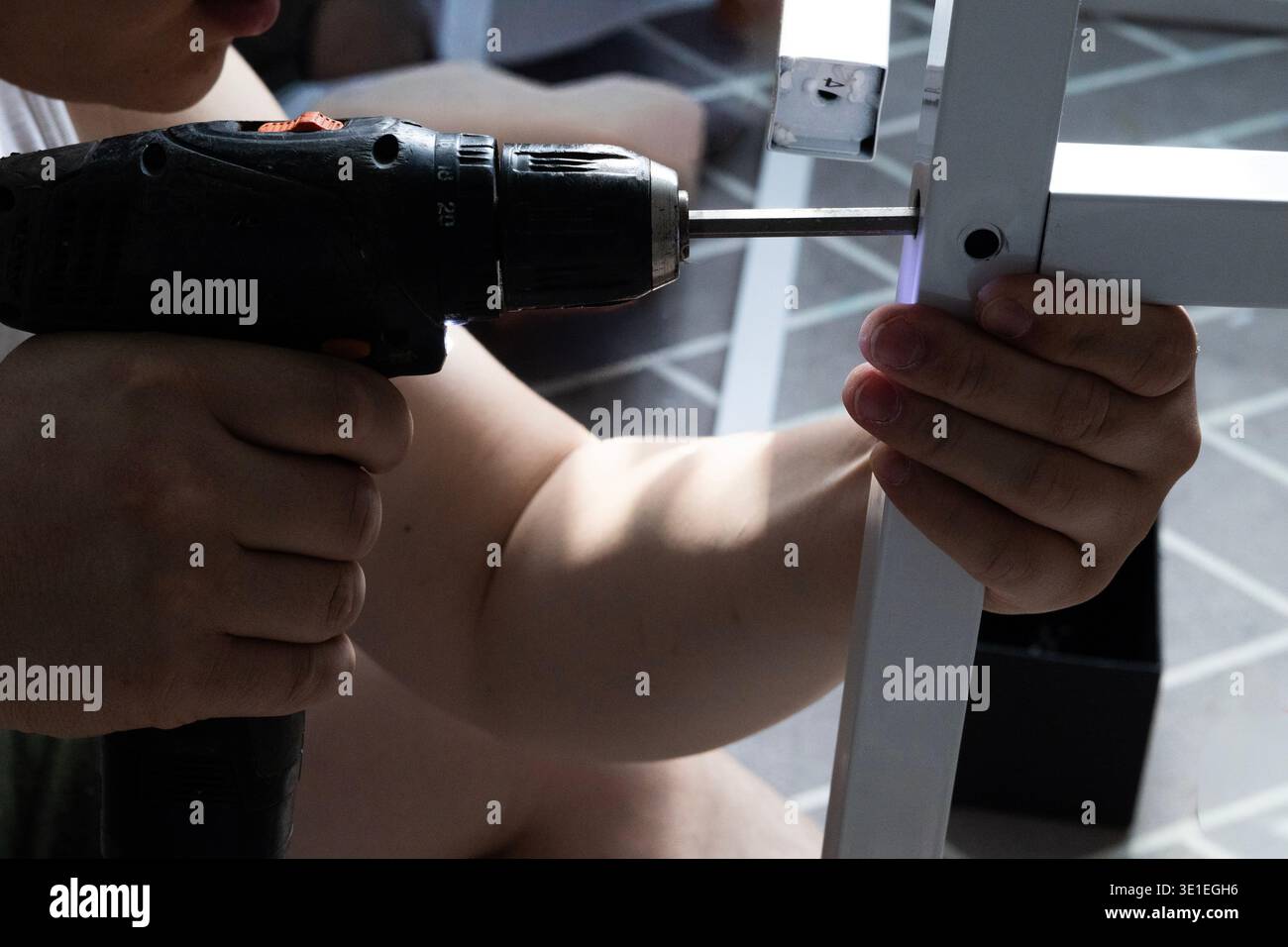 Uomo che utilizza un trapano elettrico per assemblare il telaio di mobili a casa, installazione di mobili fai da te Foto Stock