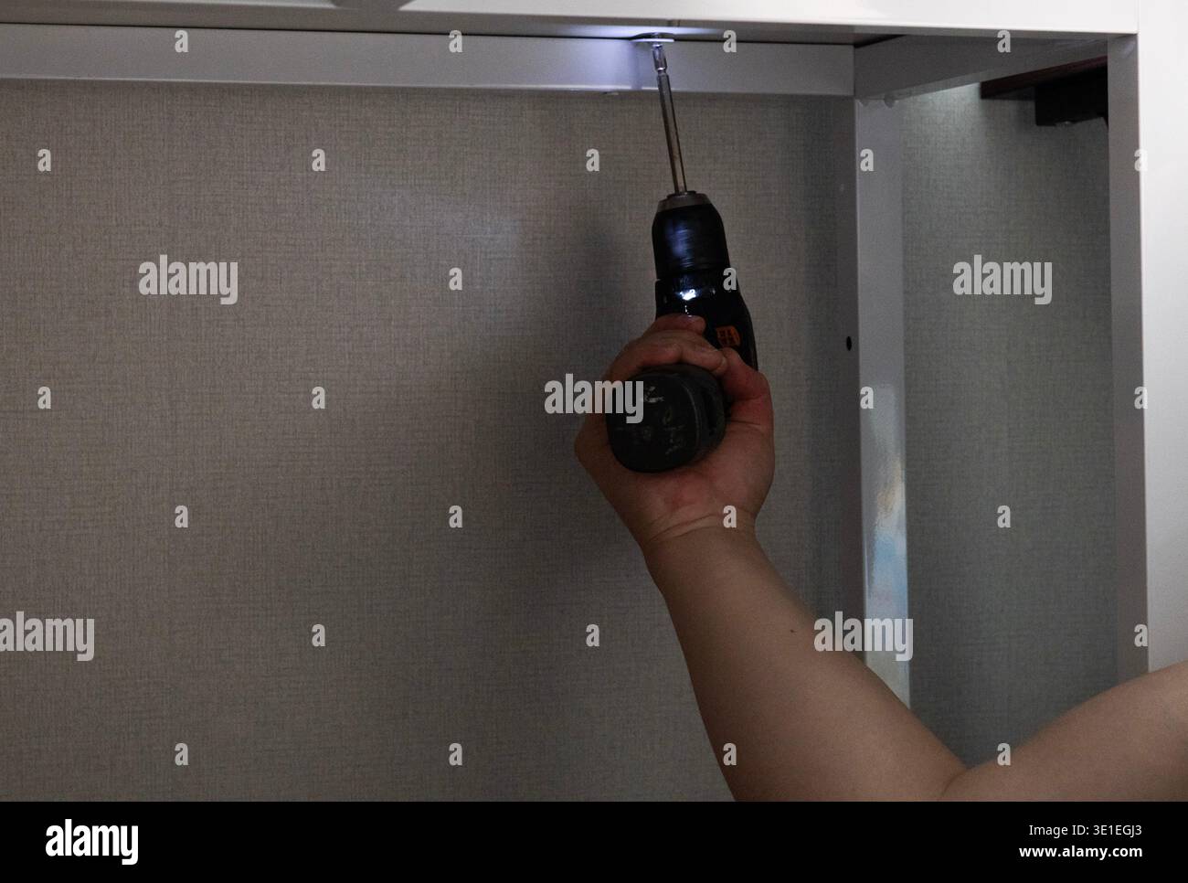 Uomo che utilizza un trapano elettrico per assemblare il telaio di mobili a casa, installazione di mobili fai da te Foto Stock