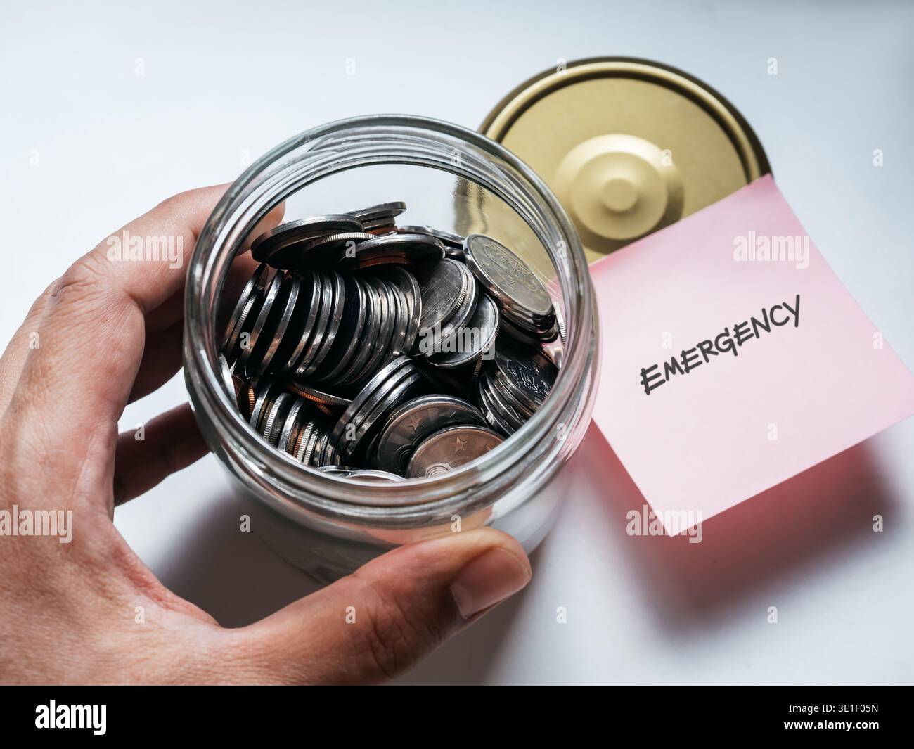 A riempito di monete in vaso di vetro etichettato emergenza sul tappo sul tavolo. Sicurezza finanziaria, budget, risparmi personali, gestione del denaro di riserva e preparazione Foto Stock