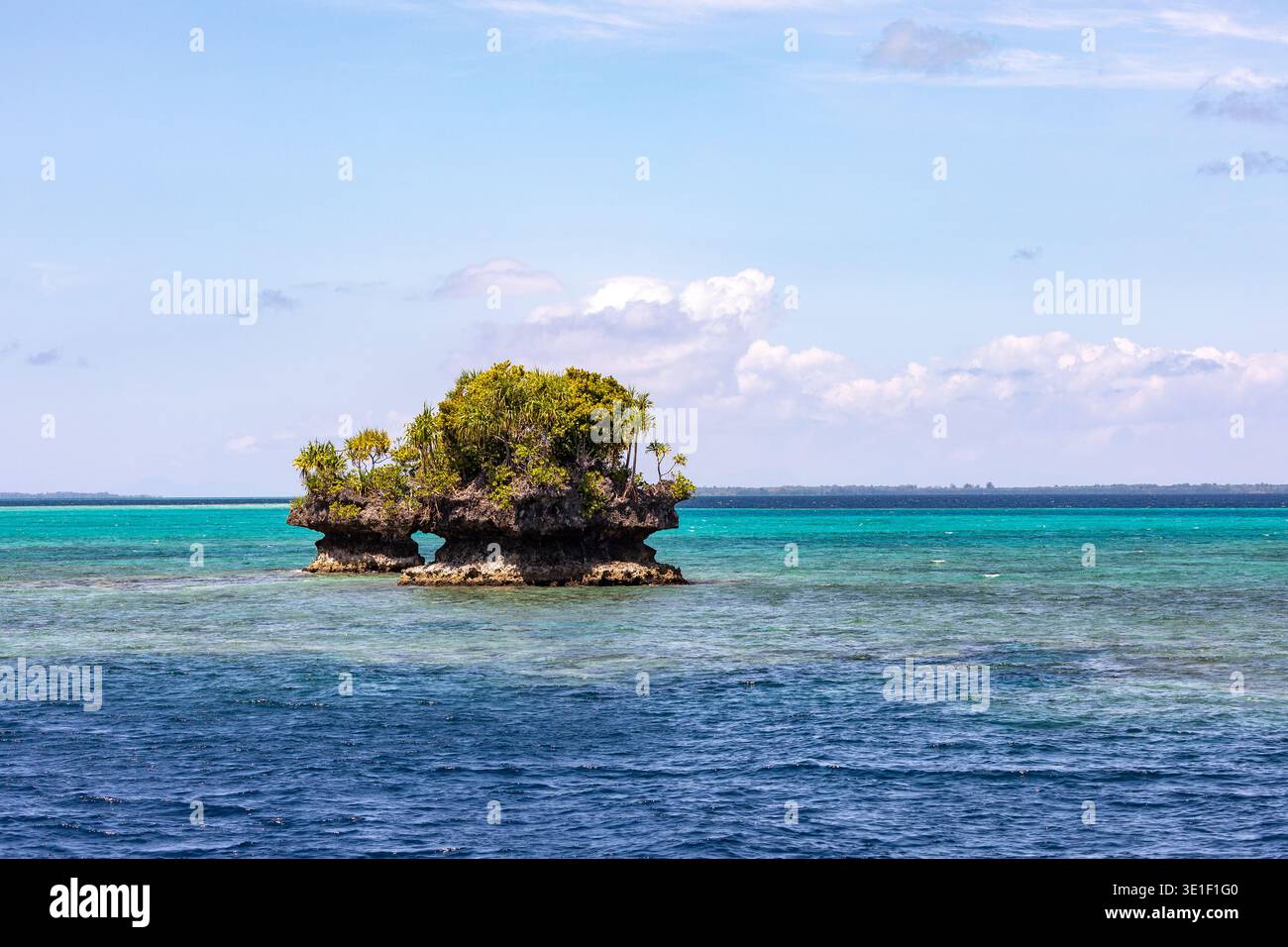Una piccola isola rocciosa coperta da lussureggiante vegetazione sorge dalle acque turchesi dell'oceano. L'isola ha un arco naturale intagliato nella sua Foto Stock