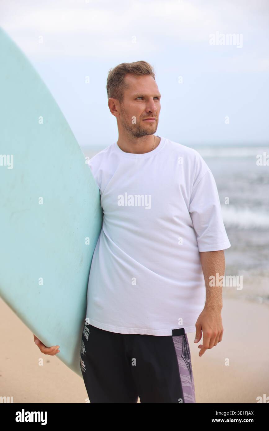 Tavola da surf. Ritratto del surfista maschile che tiene in mano la tavola da surf di Ocean Shore con sfondo in tessuto testurizzato Foto Stock