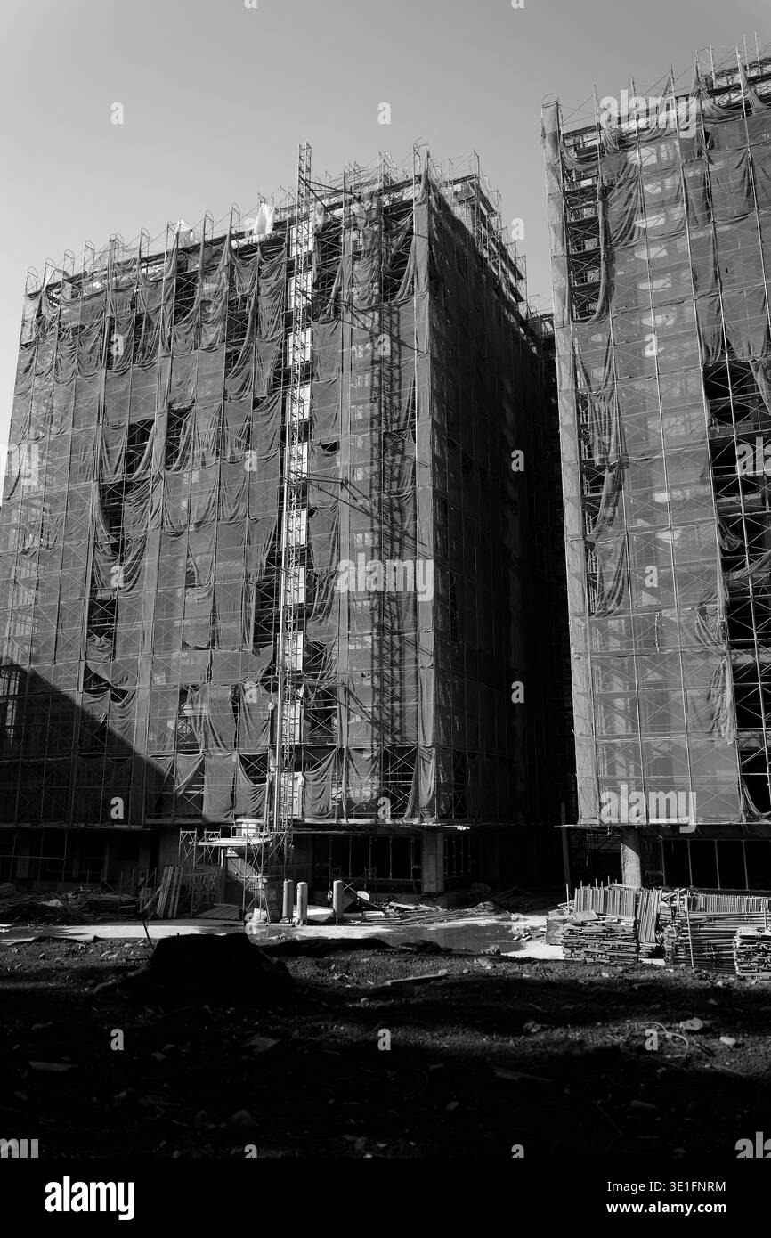 Due edifici alti in costruzione, coperti da ponteggi e teloni, che trasportano desolazione urbana e atmosfera industriale grezza. Foto Stock