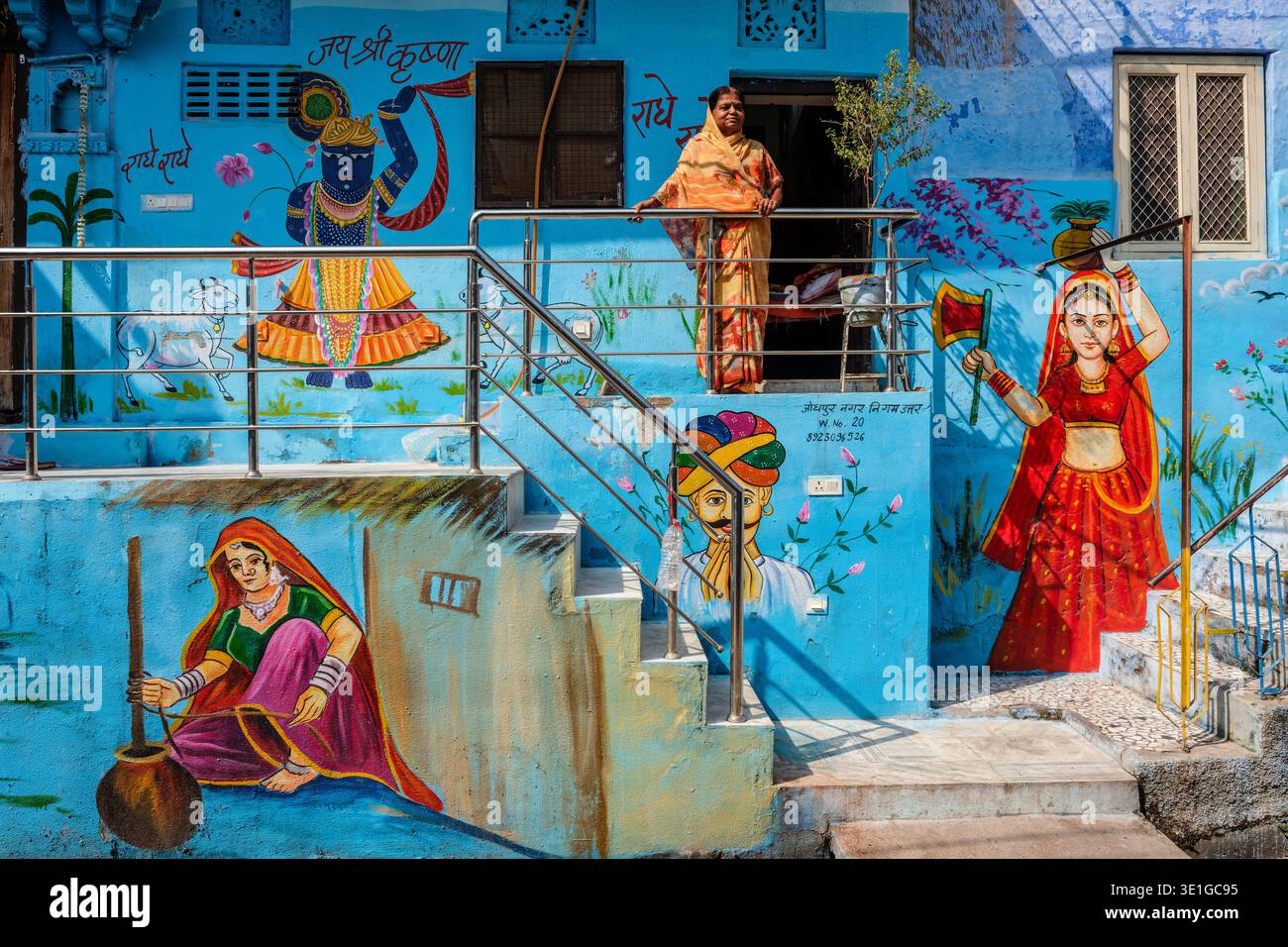 I residenti si trovano vicino agli ingressi dipinti di blu delle abitazioni di Jodhpur, decorate con pittoreschi murali di figure in abiti tradizionali. Foto Stock