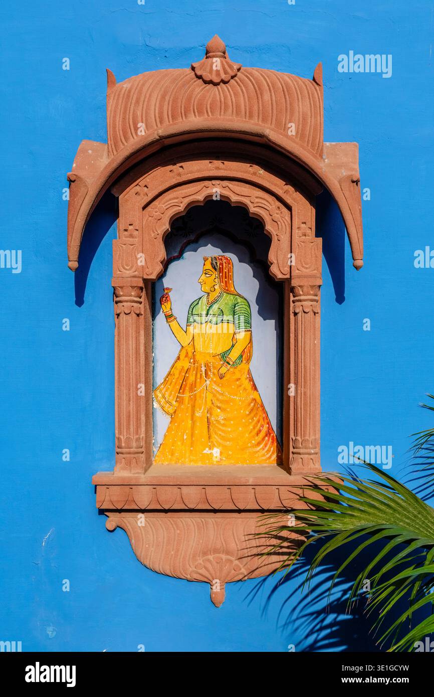 Un dipinto classico di una donna è incorniciato all'interno di una finestra di arenaria di jharokha su una parete blu brillante a Jodhpur. Foto Stock