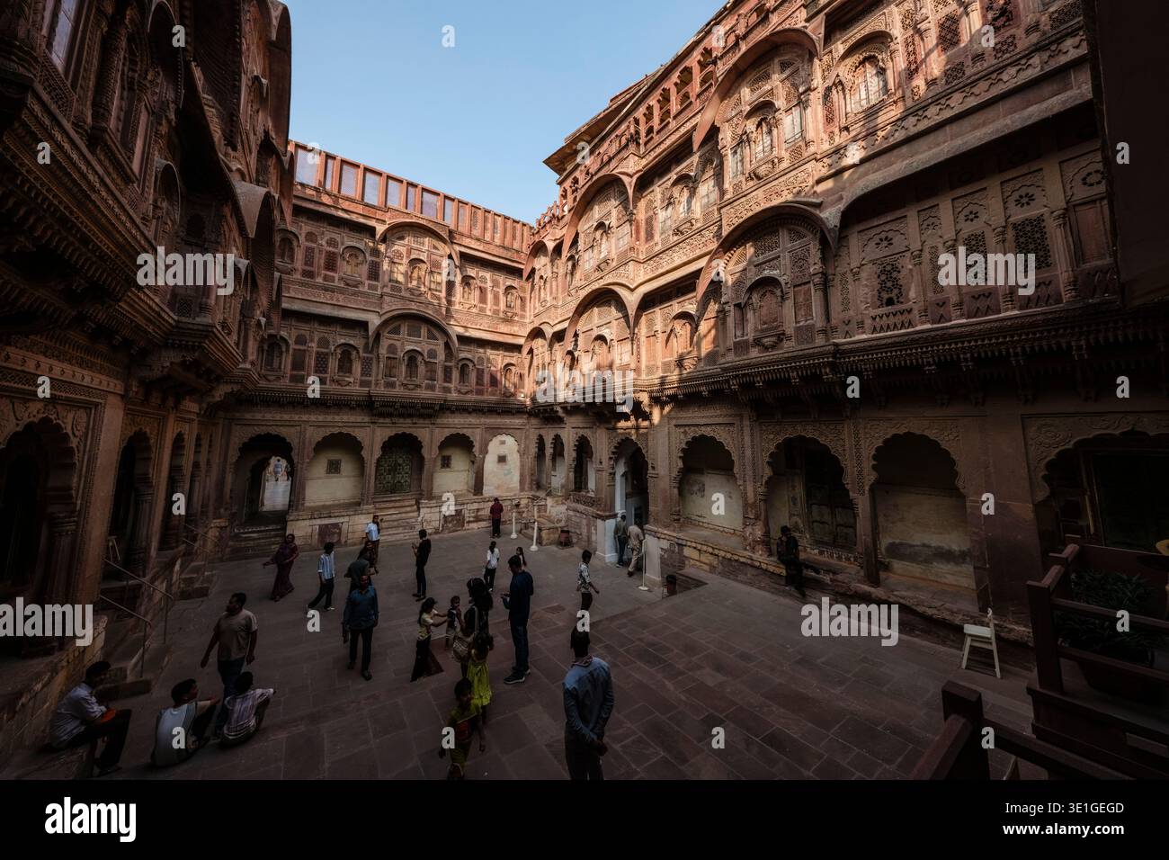 I visitatori camminano attraverso il cortile ornato in arenaria del forte Mehrangarh a Jodhpur, circondato da un'intricata architettura Rajput. Foto Stock